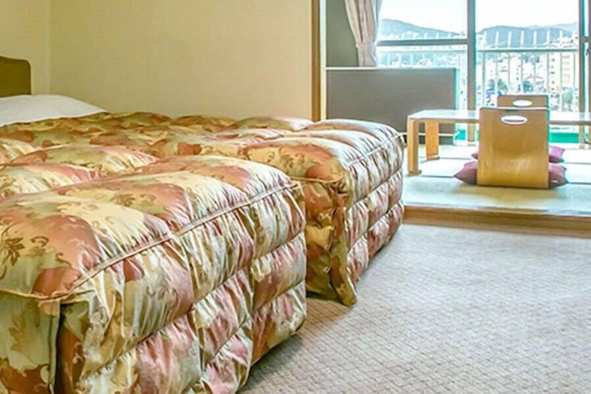 A bedroom with a large bed, a window with a view, and a small table with a bag.