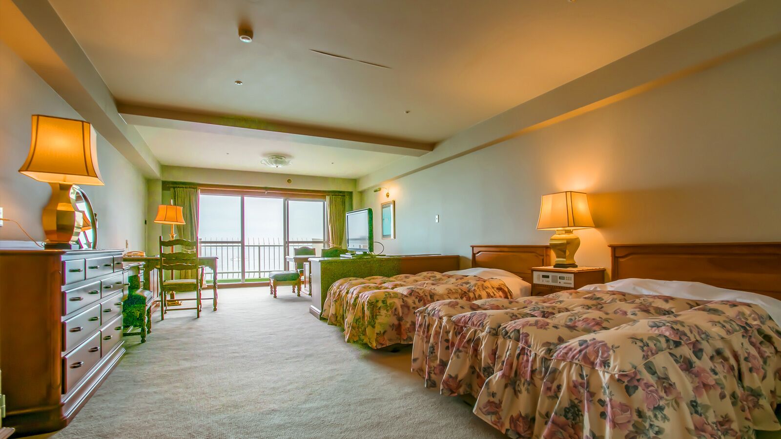 A hotel room with two beds, a desk, a chair, a dresser, and a balcony with a view.
