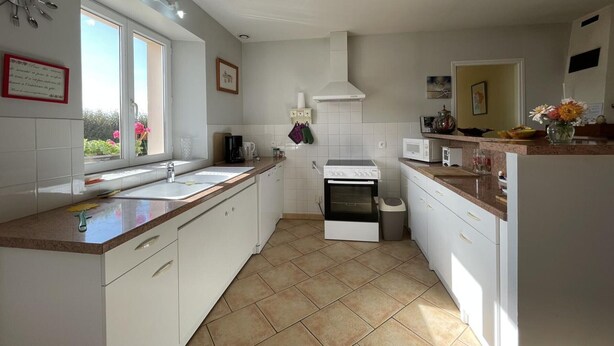 A modern kitchen with white cabinets, a built-in oven, a microwave, and a large window providing natural light. - Family stay in the heart of Perche Park (La Chapelle-Souëf)