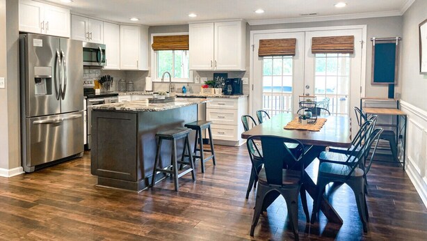 A modern kitchen with a central island, stainless steel appliances, and a dining area with a wooden table and chairs. - Fire Pit • Foosball • Trailside • Relaxing Covered Deck (Charlotte)