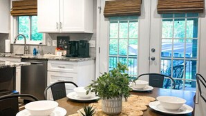 A dining area with a wooden table set for four, surrounded by white plates and bowls, with a potted plant in the center. - Fire Pit • Foosball • Trailside • Relaxing Covered Deck (Charlotte)