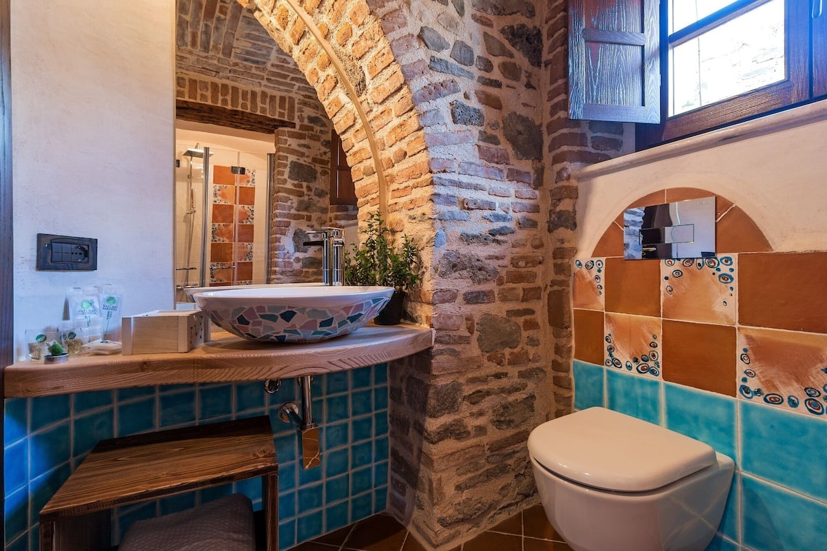 A bathroom with a stone arch, a large sink, a toilet, and a window.