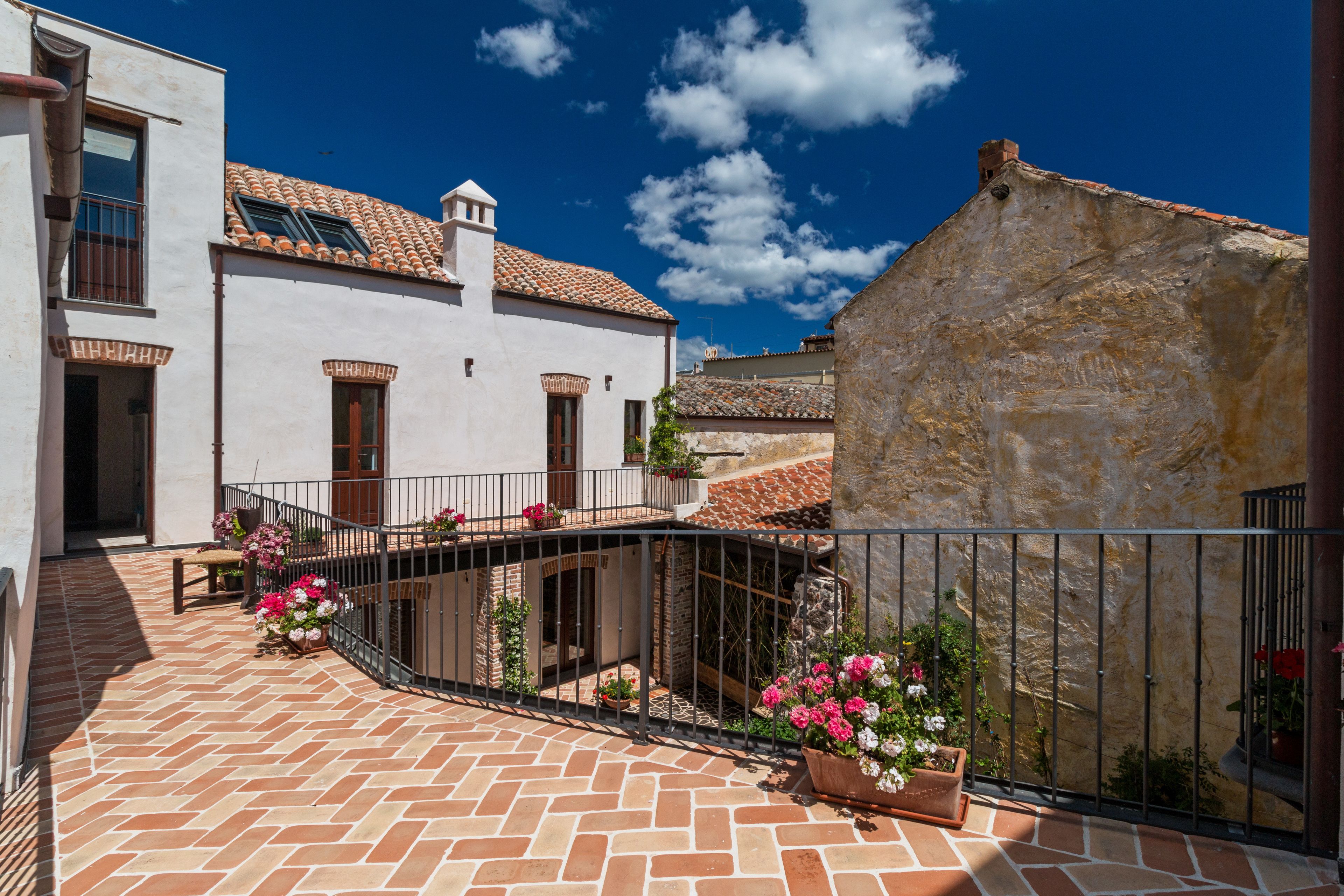 A courtyard with a tiled floor, a white building with a tiled roof, and a stone wall.