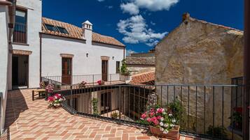 A courtyard with a tiled floor, a white building with a tiled roof, and a stone wall.
