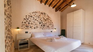 Un dormitorio con pared de piedra, cama con sábanas blancas, mesita de noche y techo de madera.
