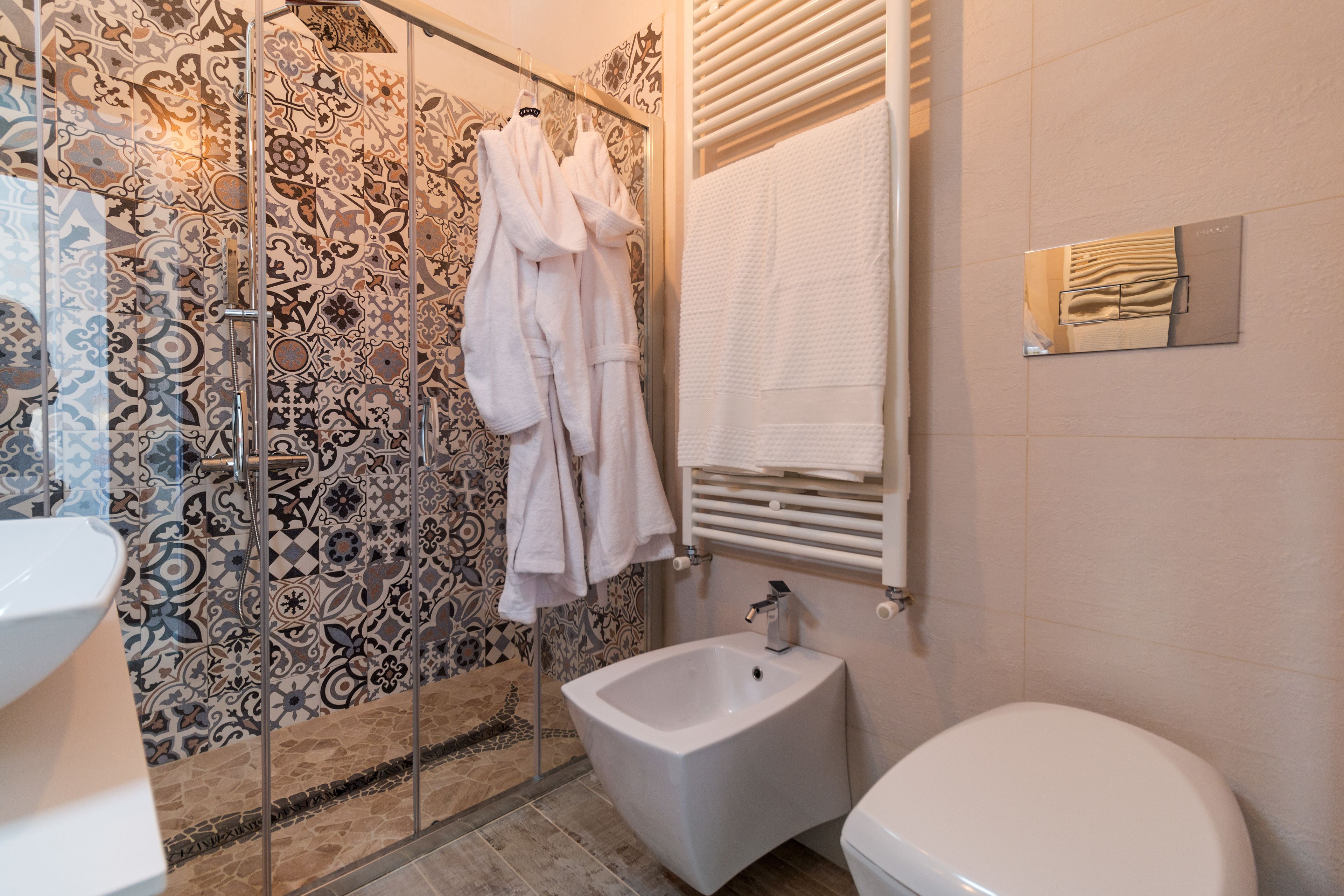 Bagno con piastrelle decorate, un bidet, un WC e accappatoi appesi.