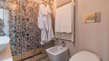 Bagno con piastrelle decorate, un bidet, un WC e accappatoi appesi.