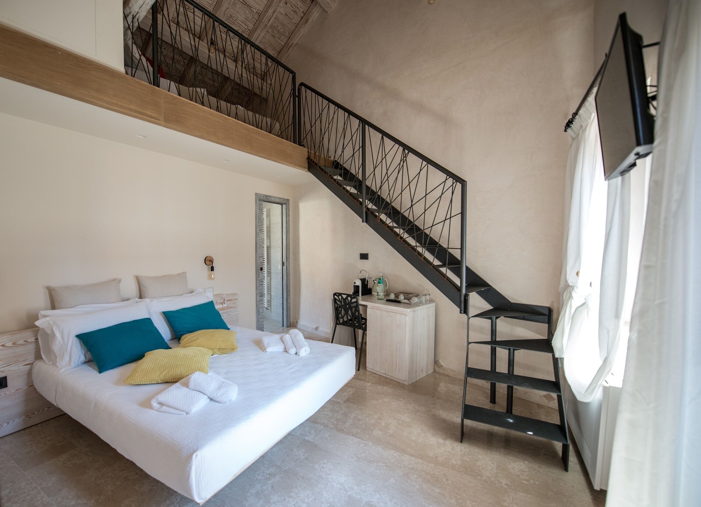 Une chambre avec un grand lit, un plafond en bois, un escalier et une petite table sur laquelle se trouve une bouilloire.