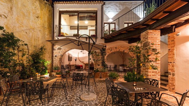 Un patio al aire libre con suelo de piedra, sillas y mesas de metal, rodeado de muros de ladrillo y plantas en macetas.