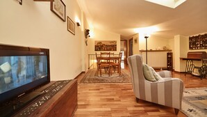 A living room with a flat-screen TV, wooden flooring, a dining area with a table and chairs, and a ceiling light. - L'Atelier (Desenzano del Garda)