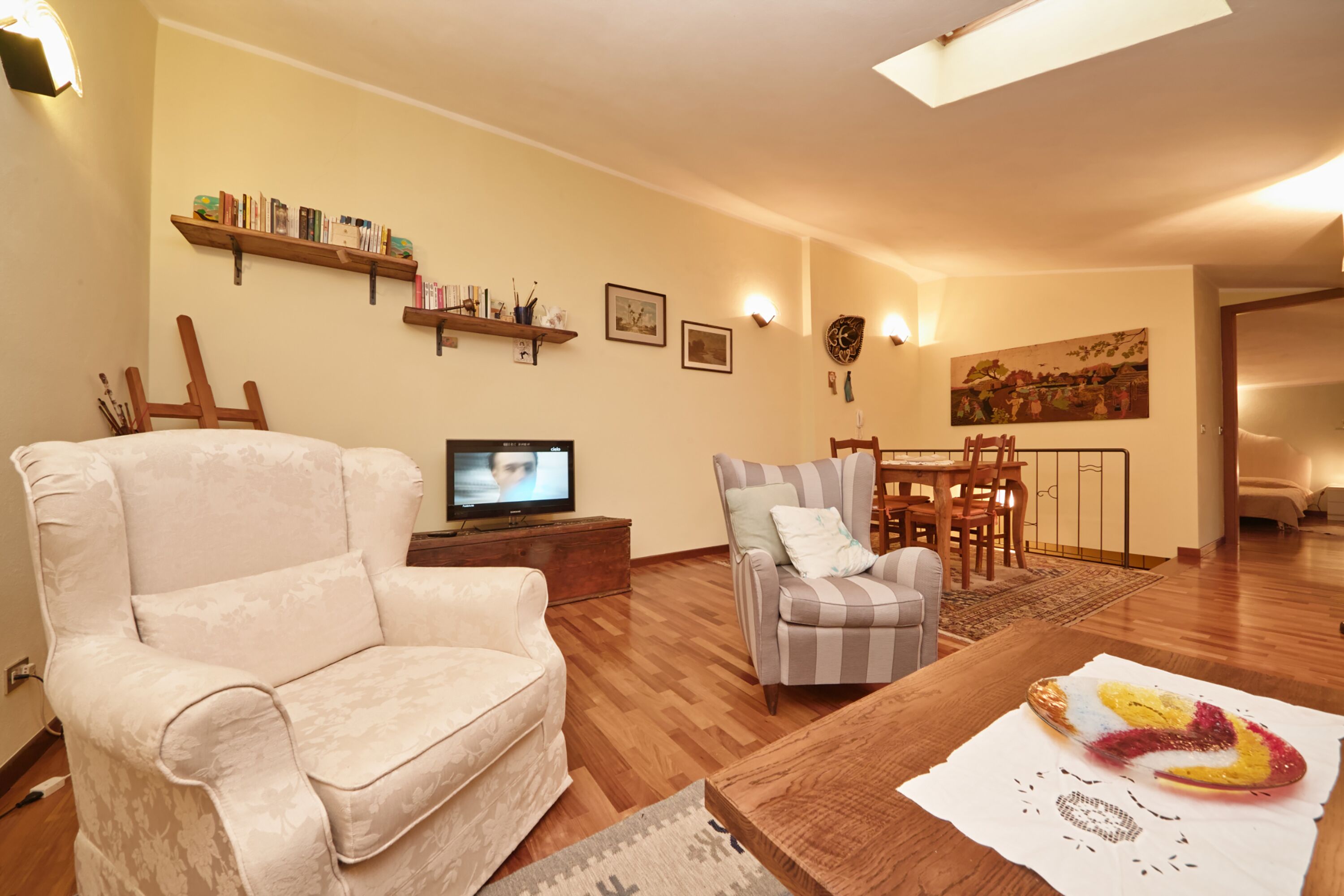 A living room with a beige armchair, a striped armchair, a wooden coffee table, and a television on a stand.