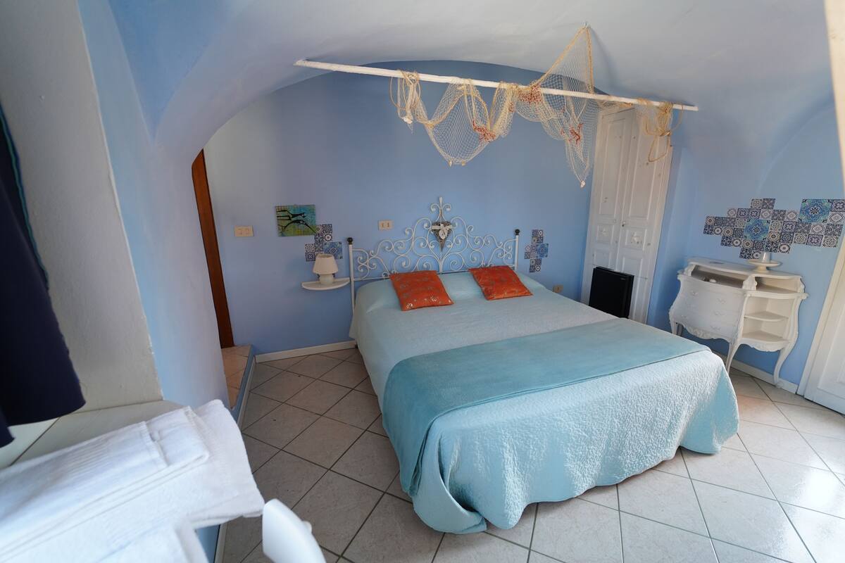 A bedroom with a bed, a hanging net, a white dresser, and a wall with decorative tiles.