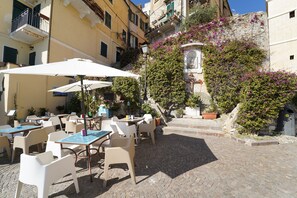 An outdoor café with tables and chairs, surrounded by cobblestone pavement and buildings with balconies. - Le Notti Mediterranee (Cervo)