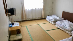 Een kamer met tatami matten, een bureau met stoel, een bed en een televisie.