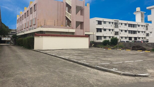 Een gebouw met een roze gevel, een aangrenzend wit gebouw en een parkeerplaats.