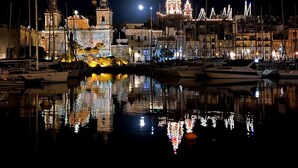 A nighttime marina with boats docked, a prominent illuminated building with a dome, and a clear reflection in the water. - BOCO Boutique (Cospicua)