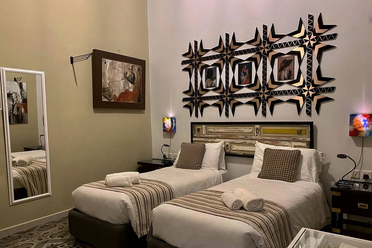 A hotel room with two beds, a large mirror, a decorative wall piece, and a TV.