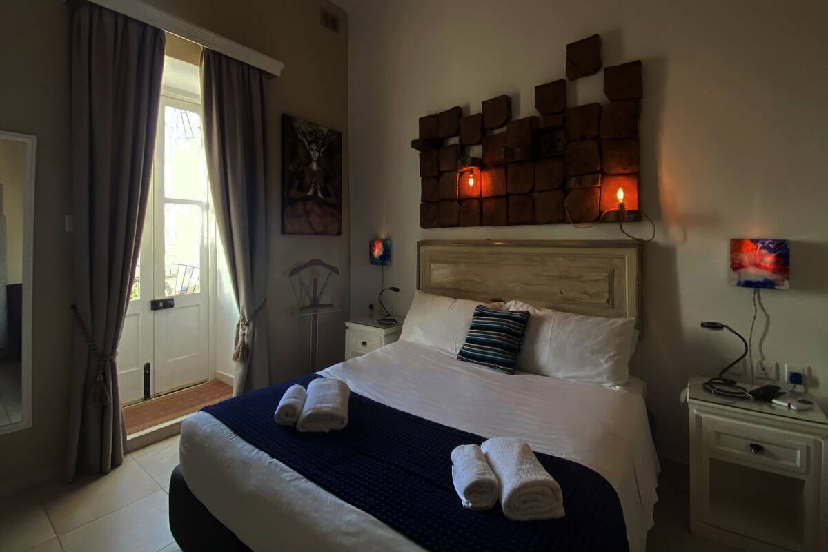 A neatly made bed with two towels, a wooden headboard, a nightstand with a lamp, and a painting on the wall.