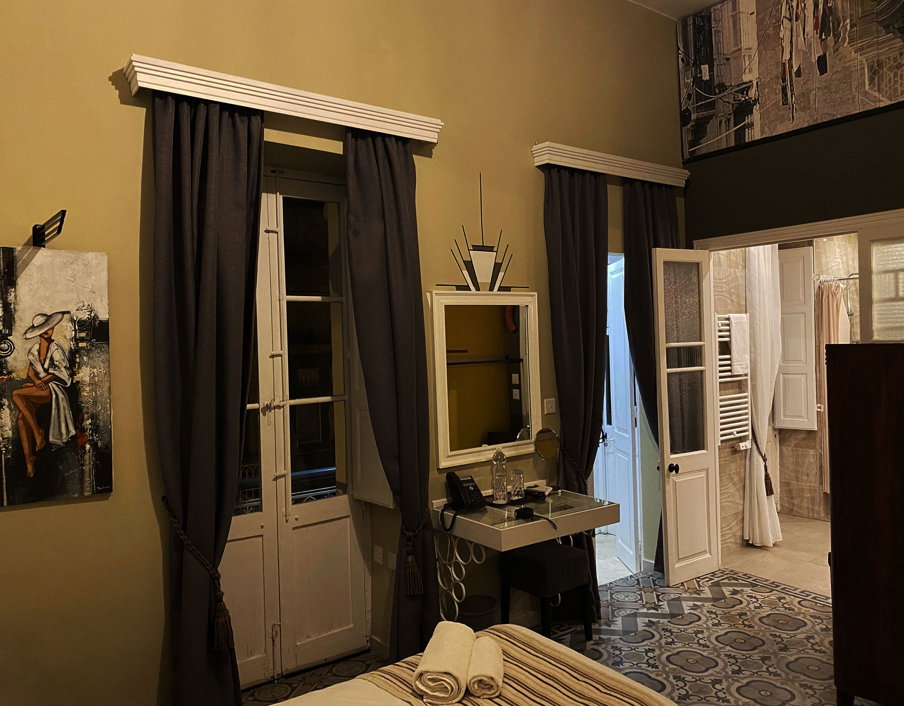 A room with a bed, a desk with a mirror, and a door leading to another room.