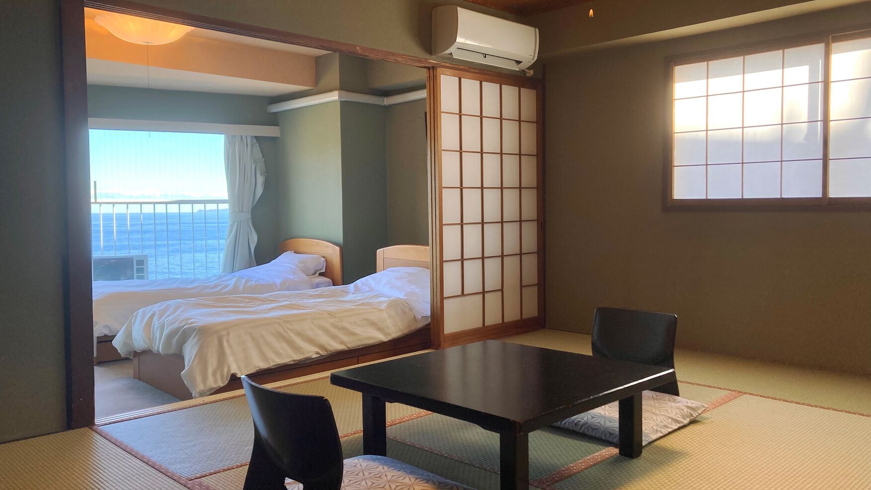 Una habitación tradicional japonesa con suelo de tatami, una mesa baja, dos camas y un shoji corredero.