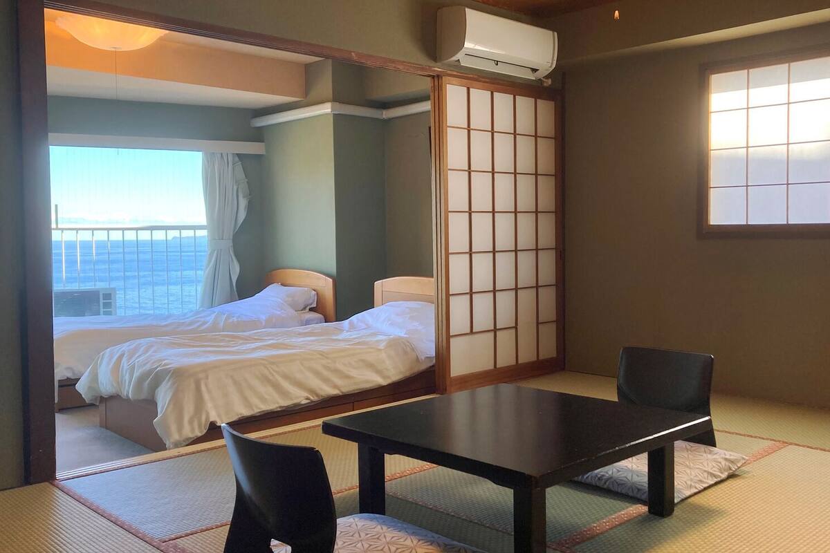 Ein traditioneller japanischer Raum mit Tatami-Boden, einem niedrigen Tisch, zwei Betten und einem verschiebbaren Shoji-Bildschirm.