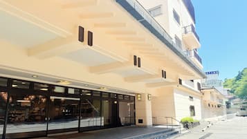 Entrada de hotel com fachada de vidro, escadaria que leva à entrada e céu claro.