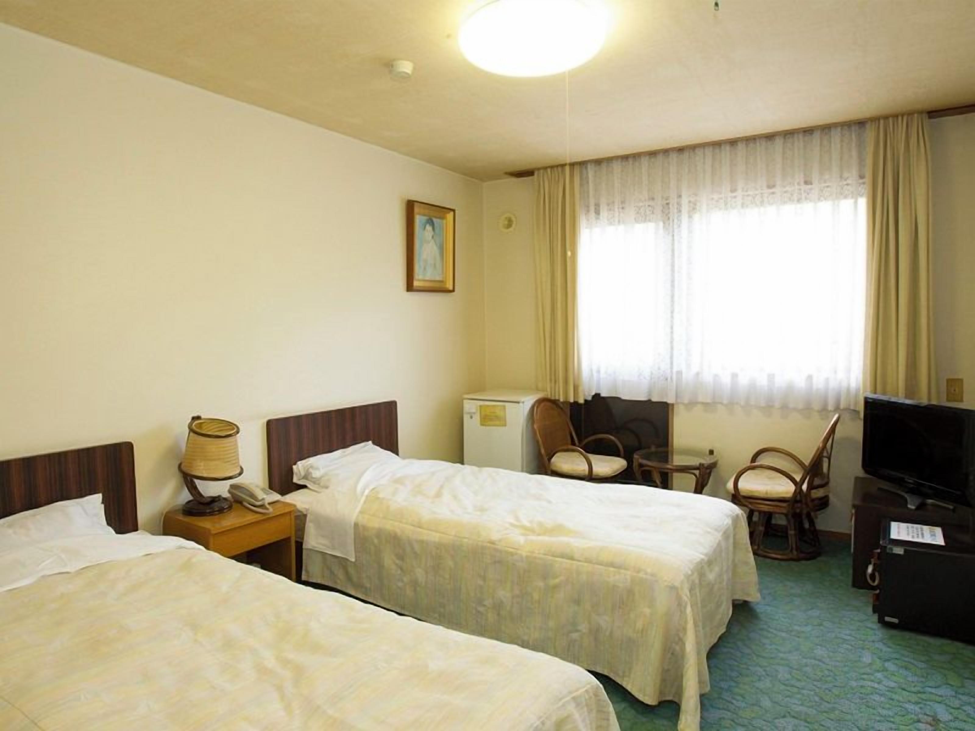 Habitación de hotel con dos camas, un escritorio, una silla, un televisor y una ventana con cortinas.