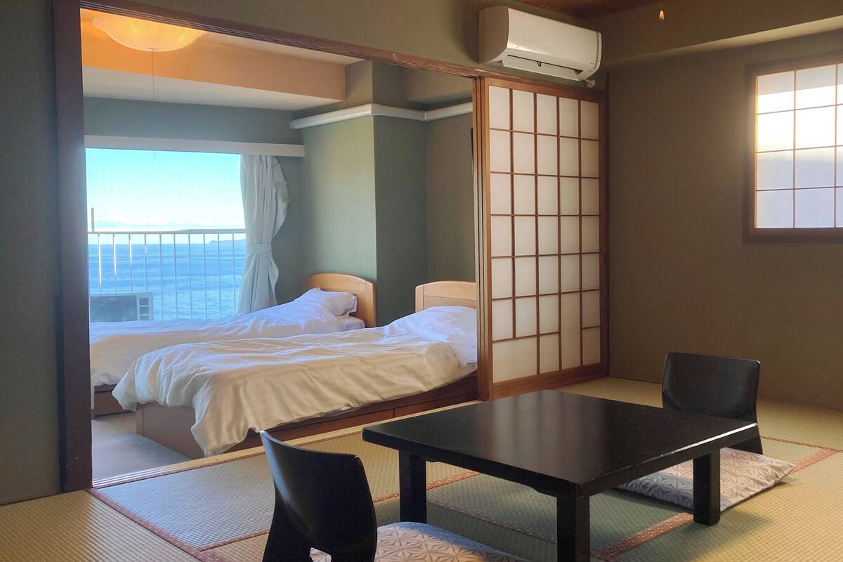 Ein Hotelzimmer mit Bett, Tisch, Stuhl, einer verschiebbaren Shoji-Schirmwand und Meerblick.