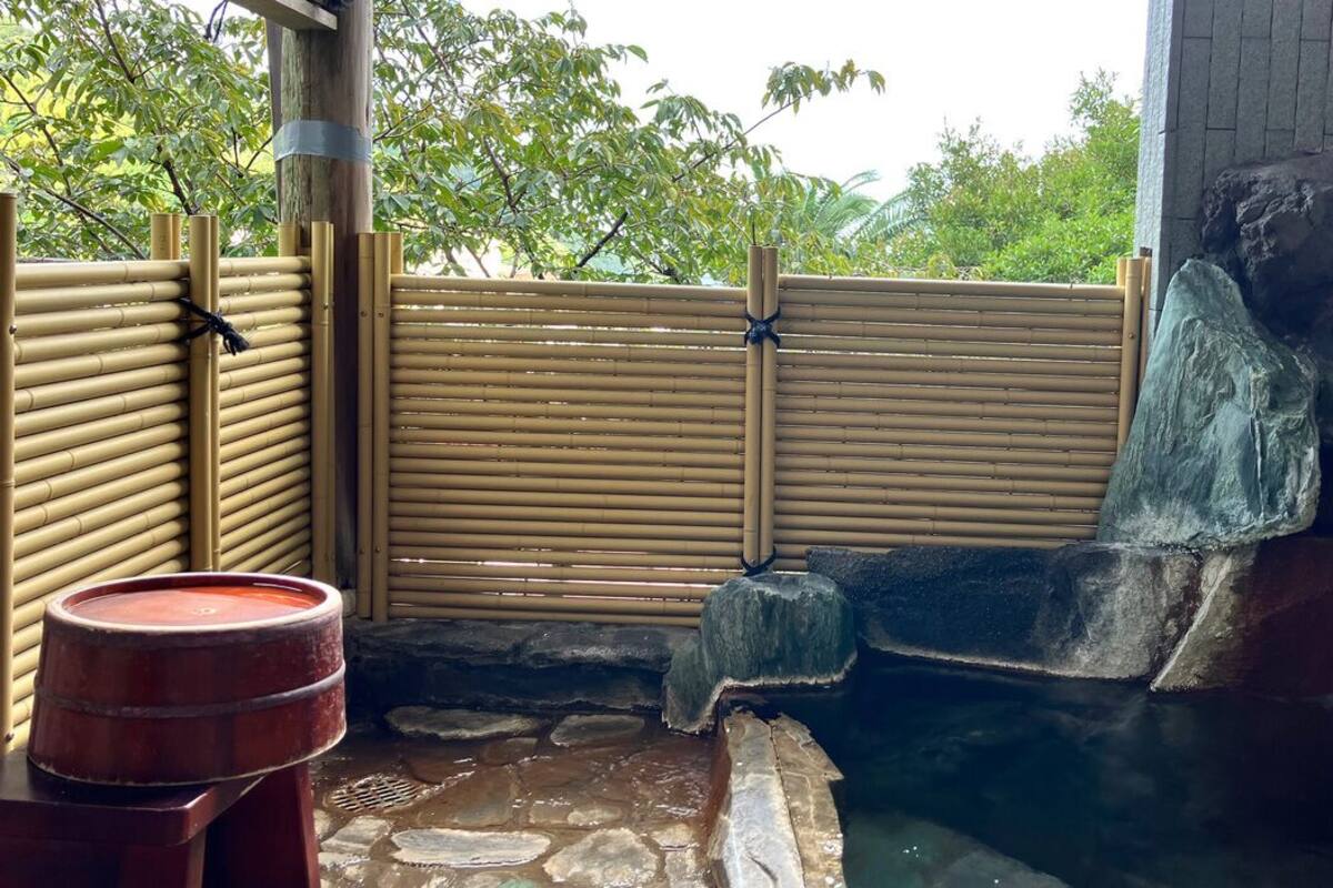 Ein traditionelles japanisches Onsen mit Bambuszaun, Steinbecken und Holzstruktur.
