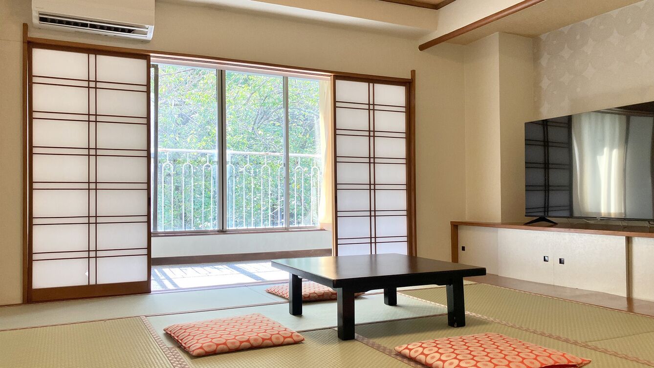 Una habitación tradicional japonesa con suelo de tatami, una puerta corredera, una mesa y un televisor.