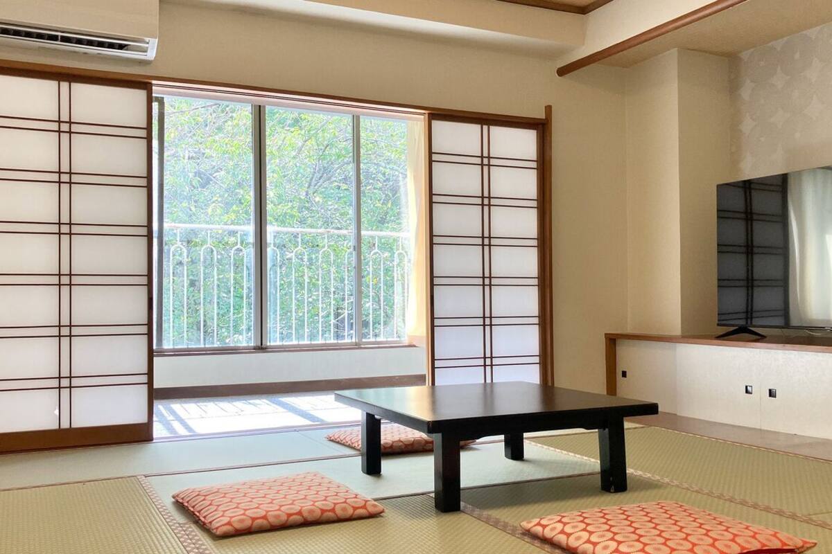 Ein traditioneller japanischer Raum mit Tatami-Bodenbelag, einer Schiebetür, einem Tisch und einem Fernseher.