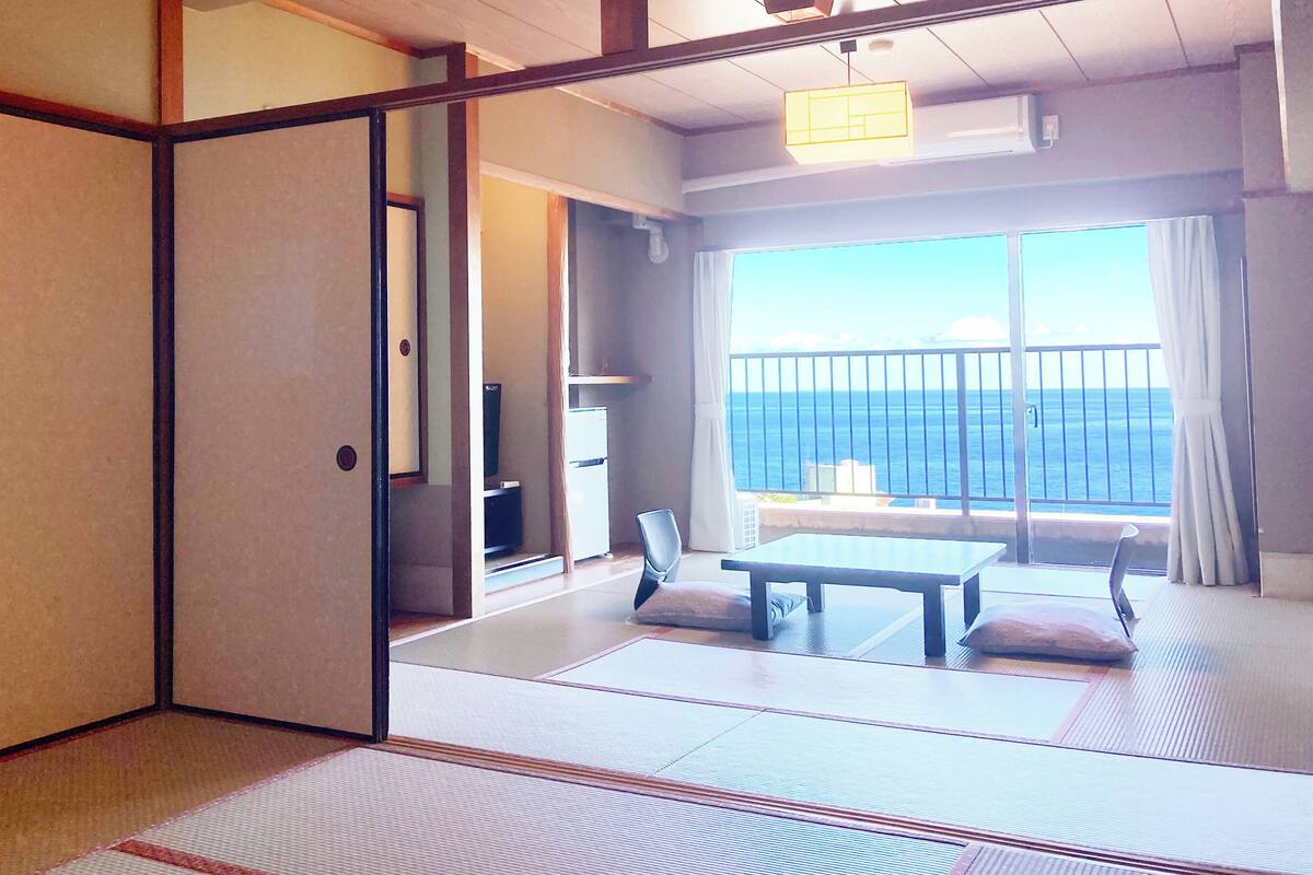 Ein traditioneller japanischer Raum mit Tatami-Boden, einer Schiebetür, einem kleinen Tisch und Meerblick.