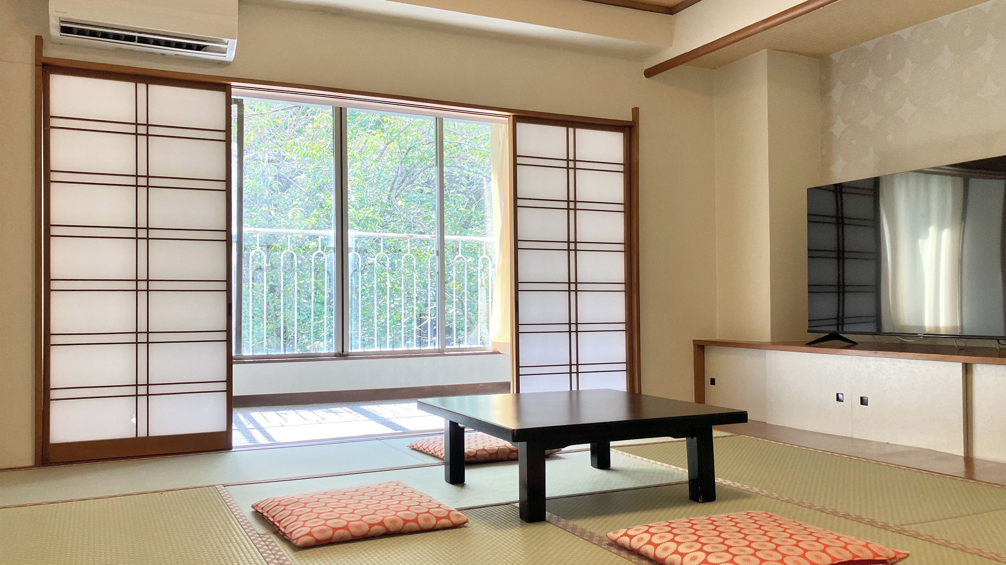 A traditional Japanese room with tatami flooring, a sliding door, a table, and a television.
