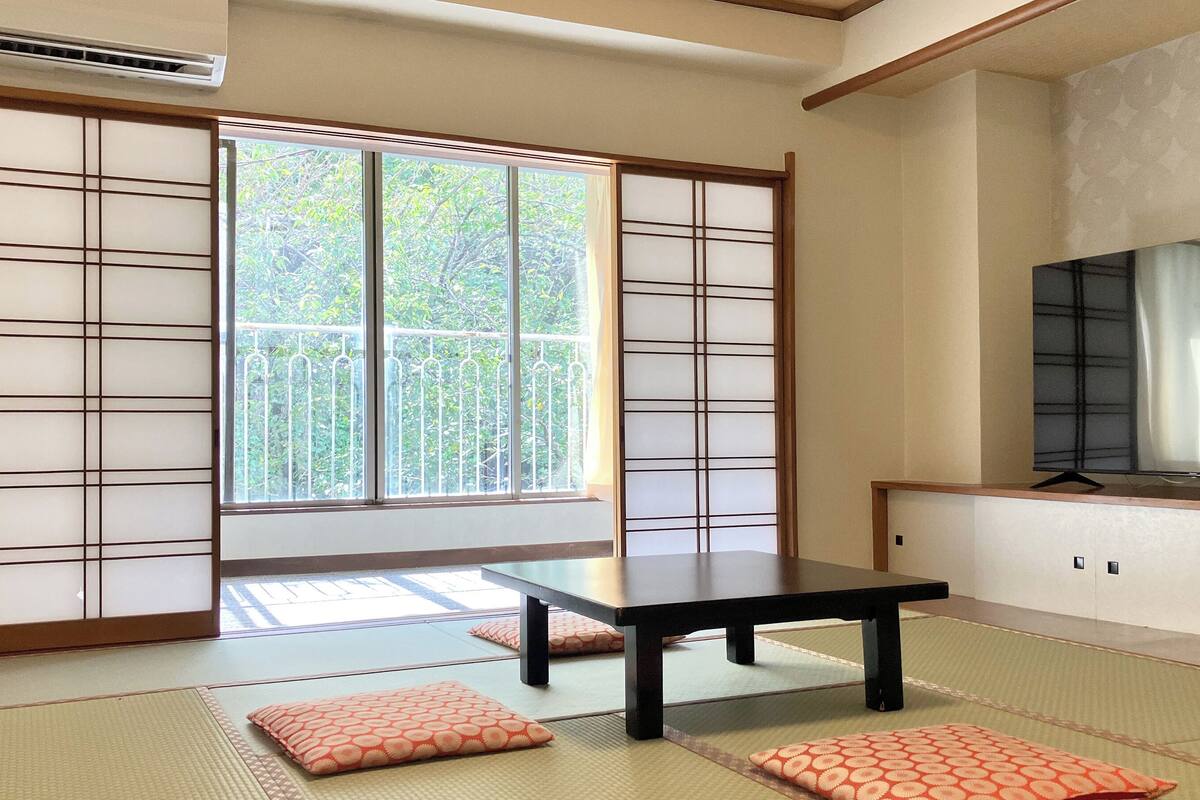 Ein traditioneller japanischer Raum mit Tatami-Böden, einer Schiebetür, einem Tisch und einem Fernseher.