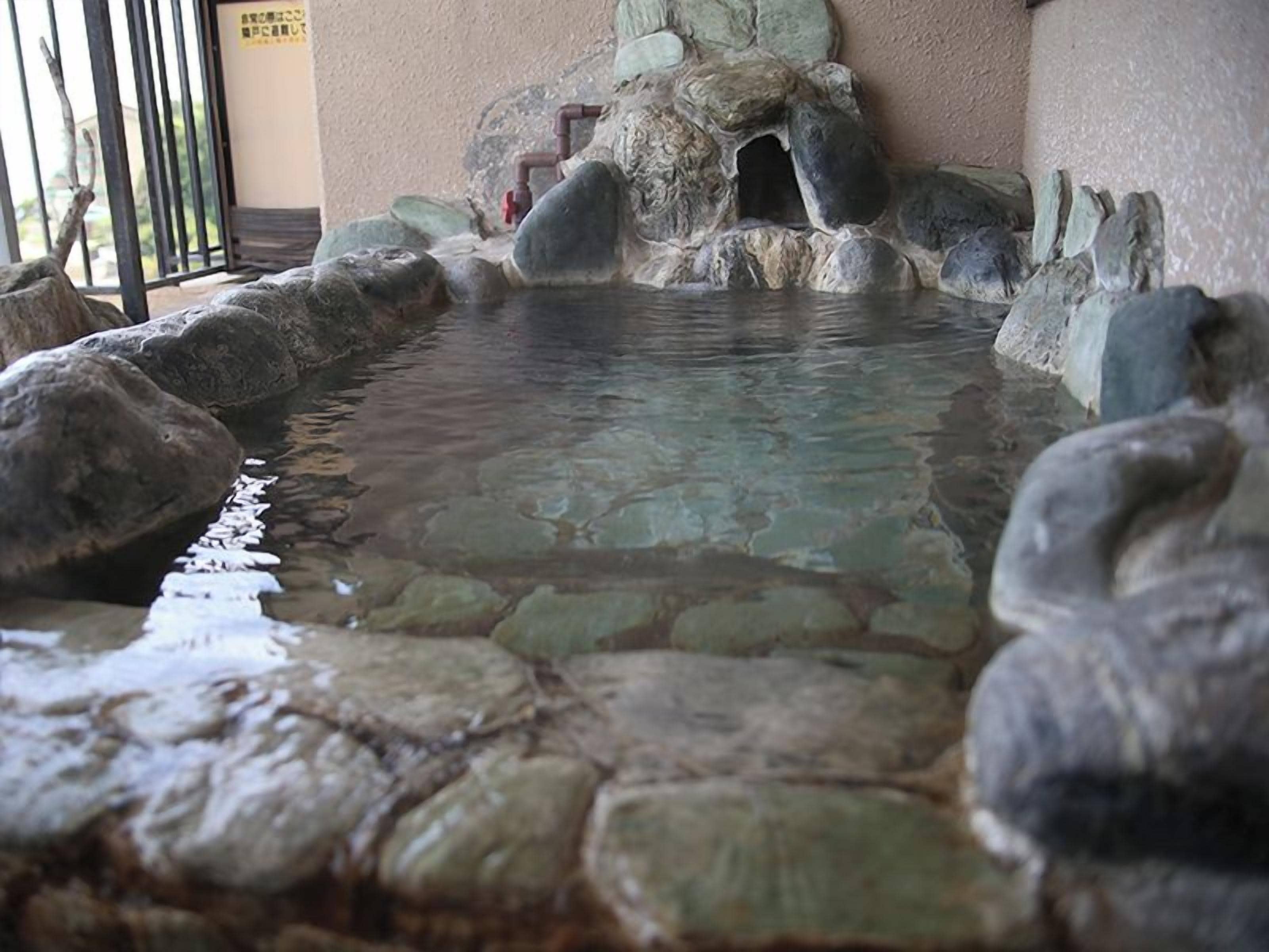A stone hot spring with a clear water surface, surrounded by rocks and a stone wall.