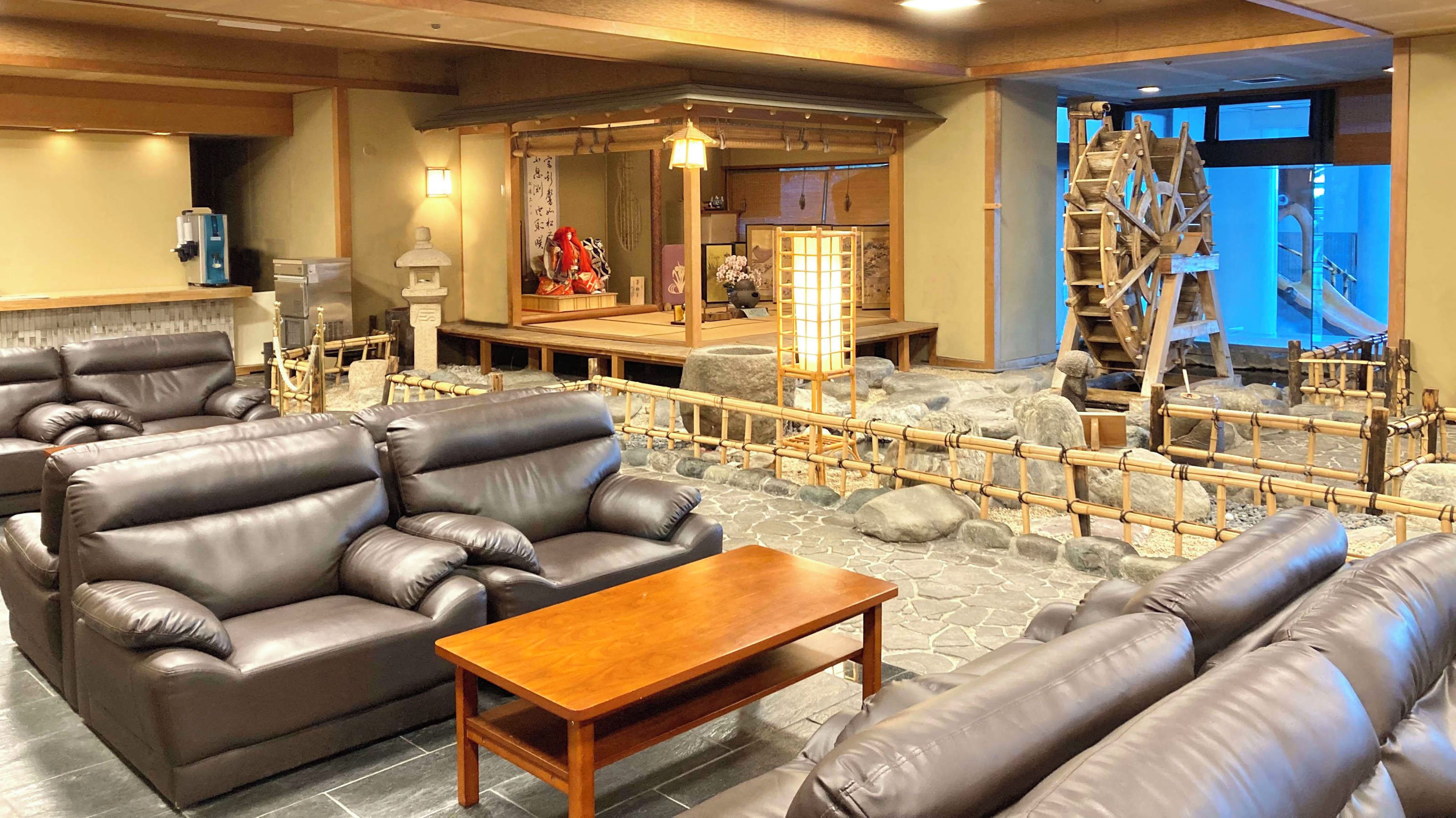 A traditional Japanese interior with tatami flooring, a tatami mat table, leather sofas, and a wooden water wheel.