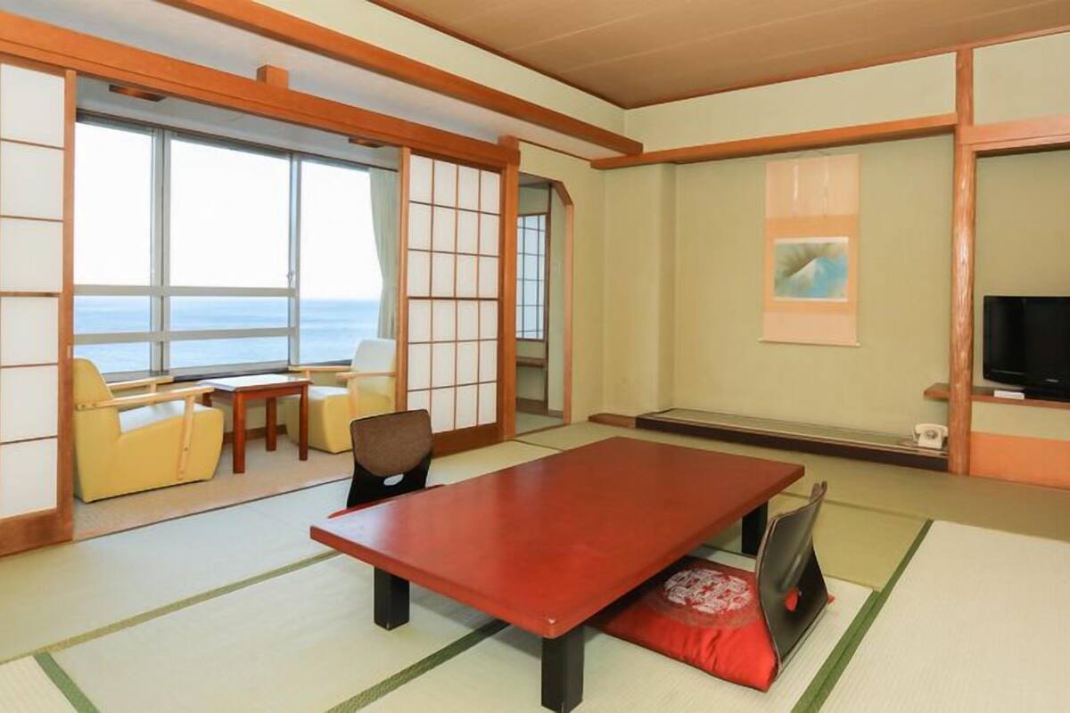 Ein traditioneller japanischer Raum mit Tatami-Bodenbelag, einem niedrigen Tisch, einer Couch und einem Fernseher.