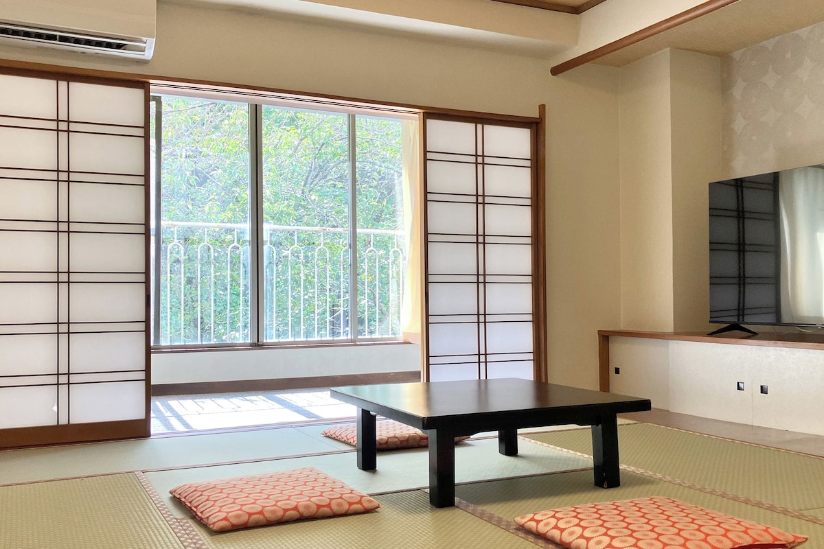 A traditional Japanese room with tatami flooring, a sliding door, a table, and a television.