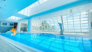 An indoor swimming pool with a slide, large windows, and a statue. - Itoen Hotel Atagawa (Higashiizu)
