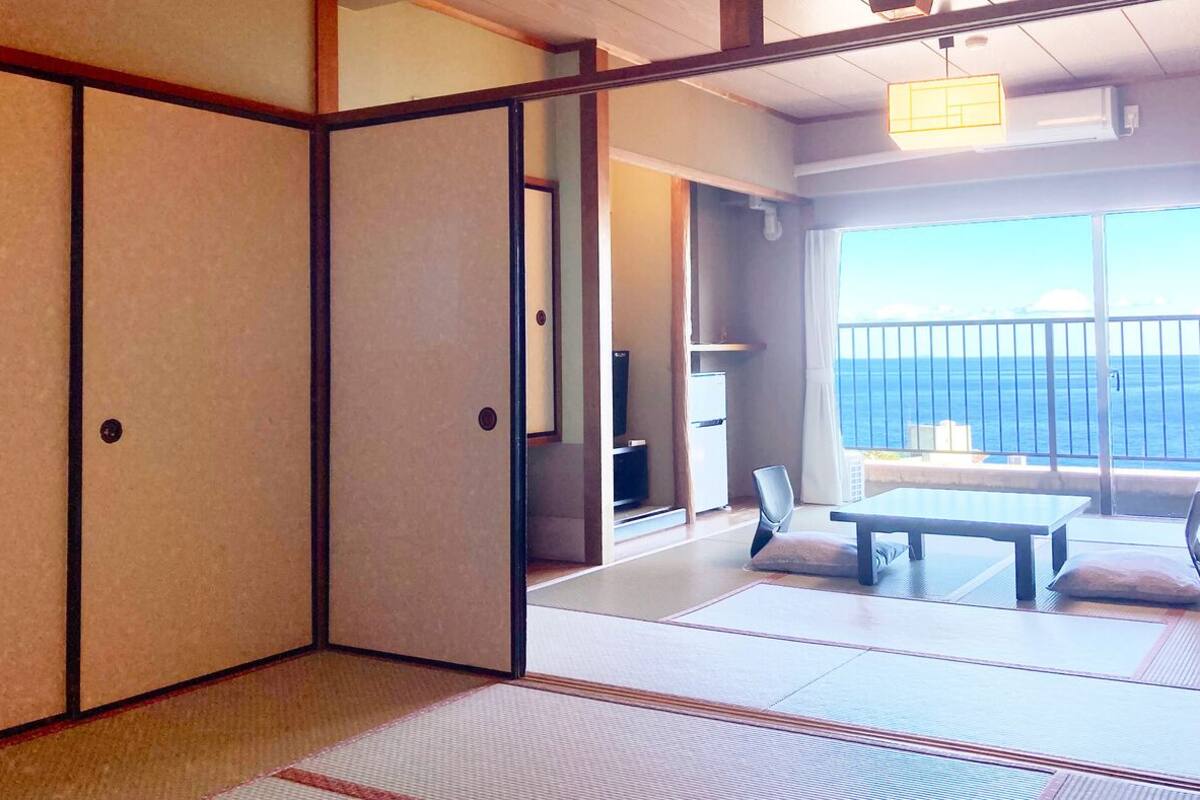 Ein traditioneller japanischer Raum mit Tatami-Bodenbelag, einer Schiebetür, einem Tisch und Blick auf das Meer.
