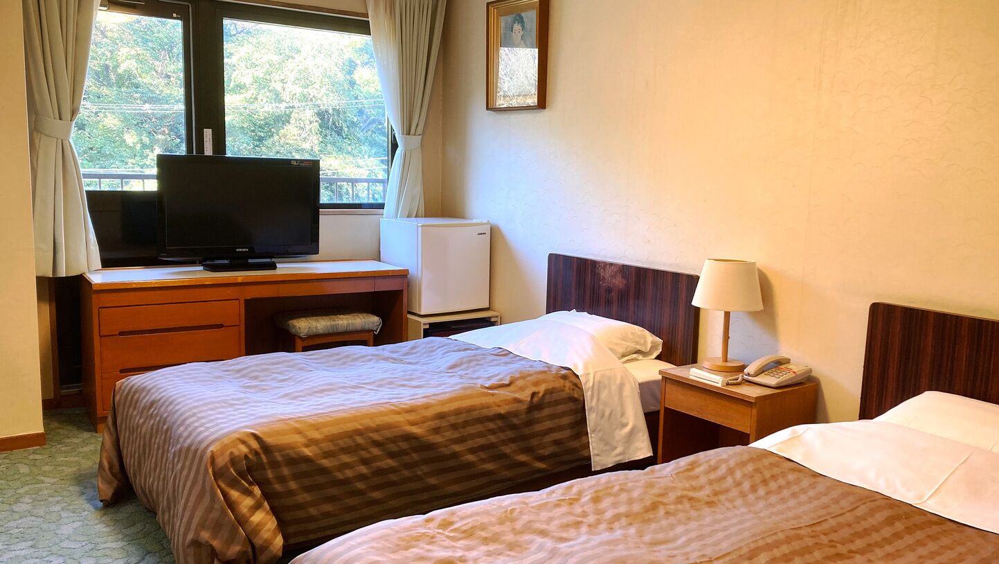 A hotel room with two beds, a desk with a television, a small refrigerator, a bedside lamp, and a telephone.