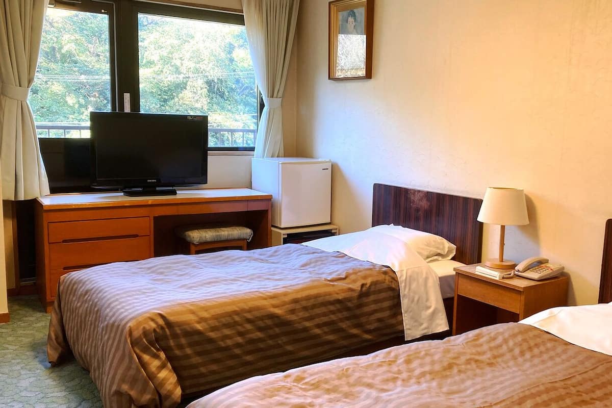 Ein Hotelzimmer mit zwei Betten, einem Schreibtisch, einem Fernseher, einer kleinen Kühlbox, einer Nachttischlampe und einem Telefon.