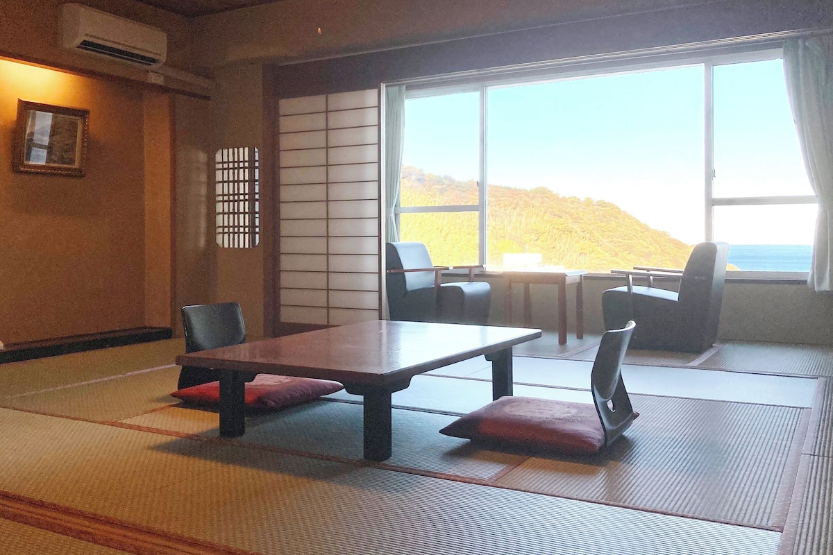 Ein traditioneller japanischer Raum mit Tatami-Boden, einem niedrigen Tisch mit Kissen und einem verschiebbaren Shoji-Bildschirm.