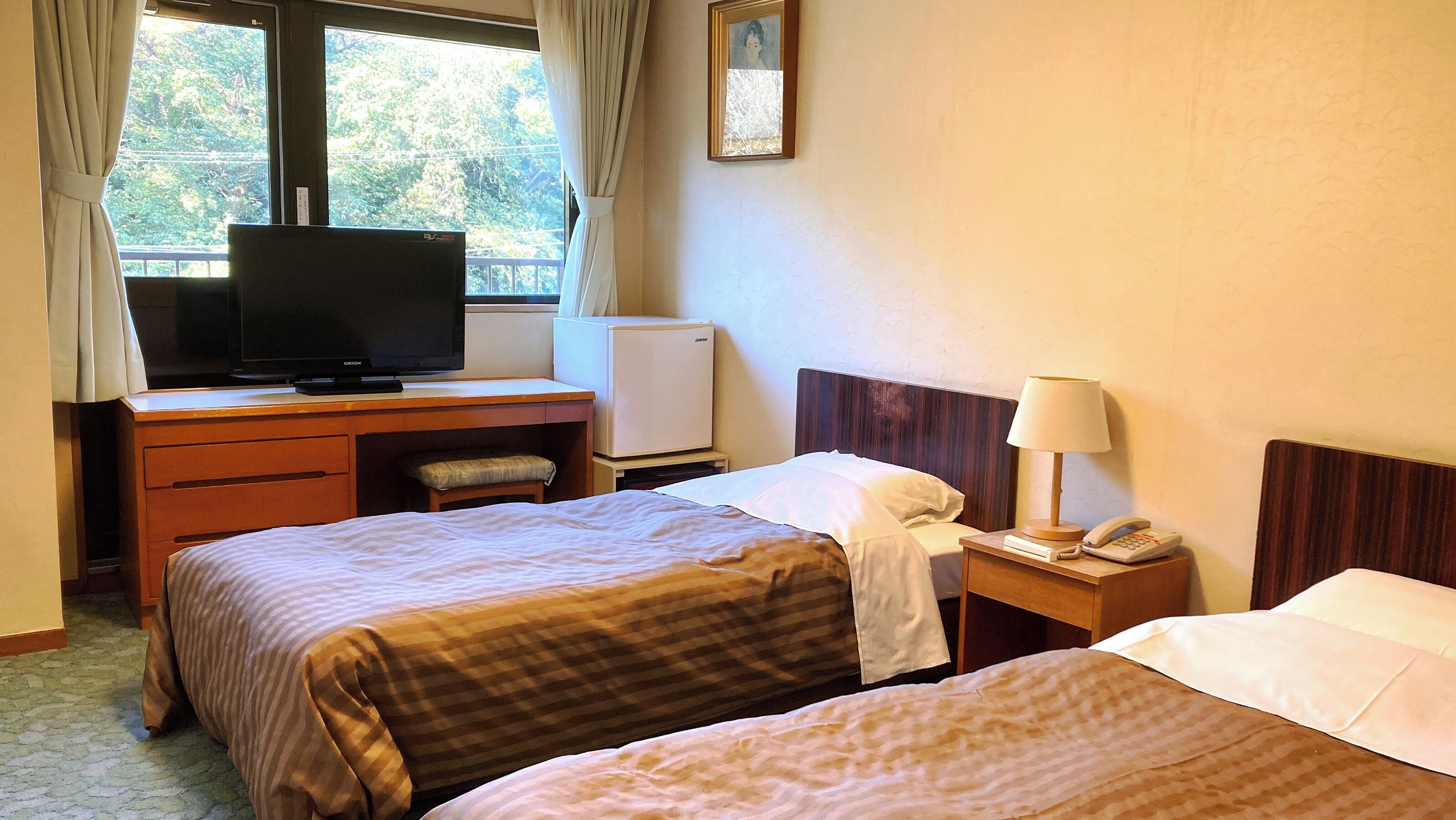 A hotel room with two beds, a desk with a television, a refrigerator, a bedside table with a lamp and phone, and a window with curtains.