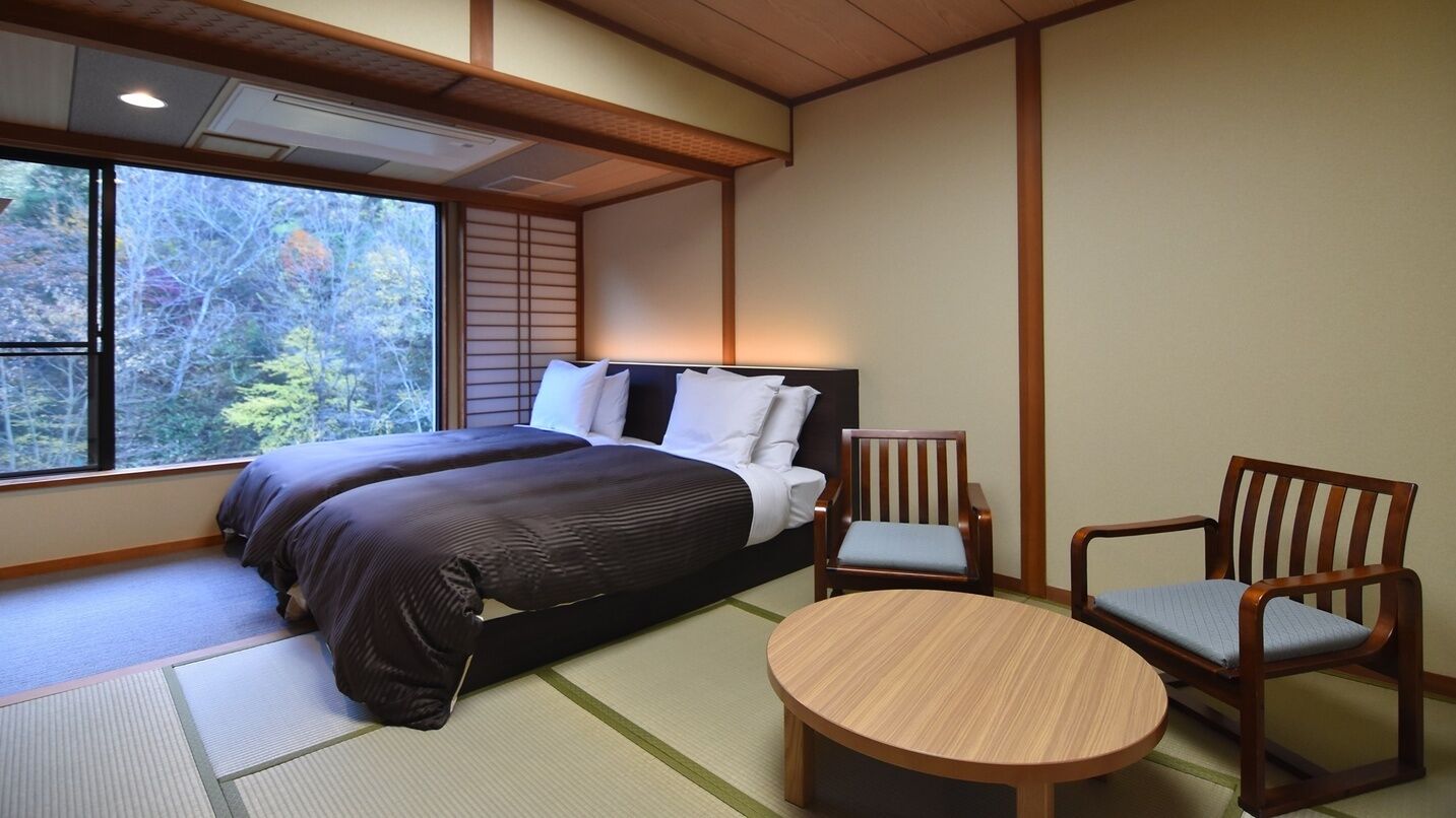 A room with a bed, two chairs, a round table, and a large window.