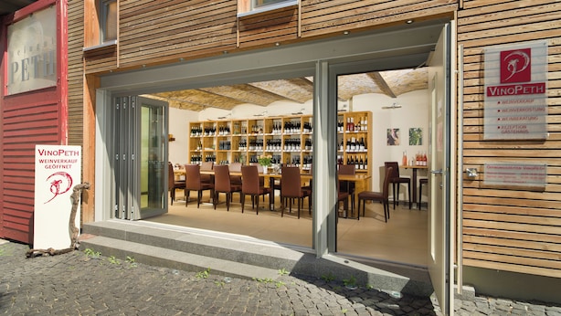 A wine shop with wooden shelves stocked with bottles, a reception desk, and a seating area with chairs. - Gästehaus und Weingut Peth (Floersheim Dalsheim)