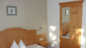 Ein Schlafzimmer mit hölzernem Kopfteil, einem Bett mit weißen Bettbezügen, einem Nachttisch, einem Holzschrank und einem gerahmten Bild an der Wand.