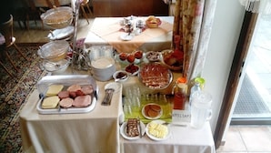 Ein reichhaltiges Buffet mit verschiedenen Speisen, darunter Fleisch, Obst und Kuchen, sowie Geschirr und eine Wasserkaraffe.