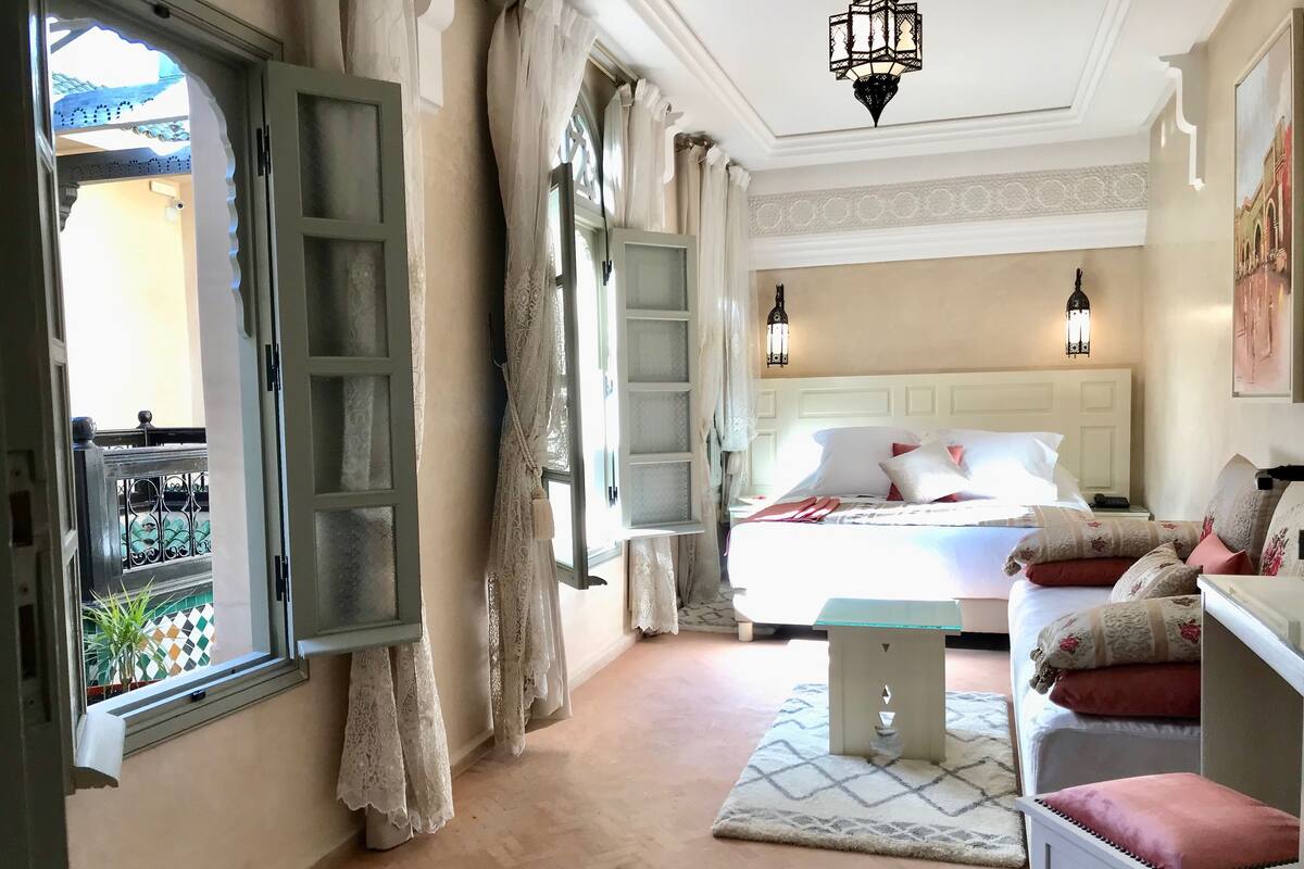 A bedroom with a bed, bedside tables, a nightstand, a window with curtains, and a view of the outside.