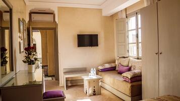 A well-lit room with a sofa, a television mounted on the wall, and a window with curtains.